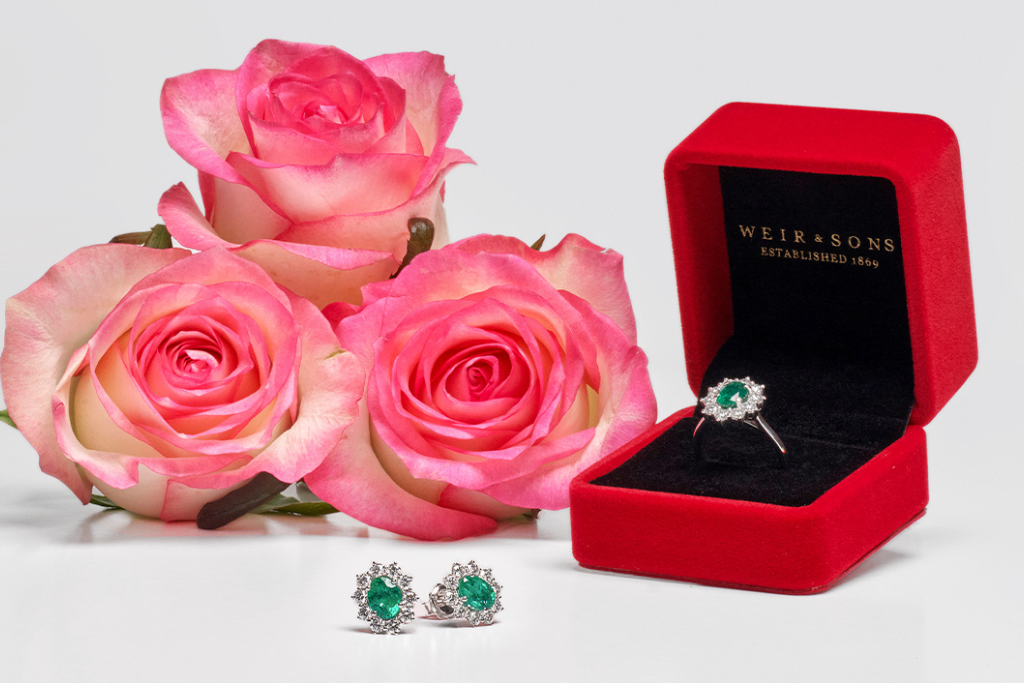 A ring in a Weir & Sons ring box, earrings and some pink roses.